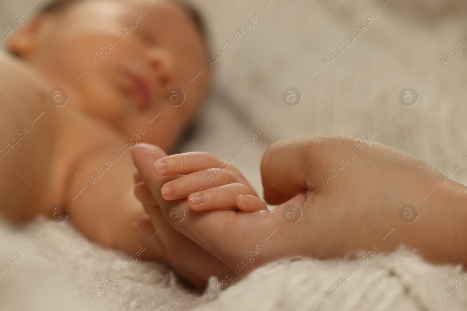 Photo of Mother holding hand of her newborn baby on beige blanket, closeup. Lovely family