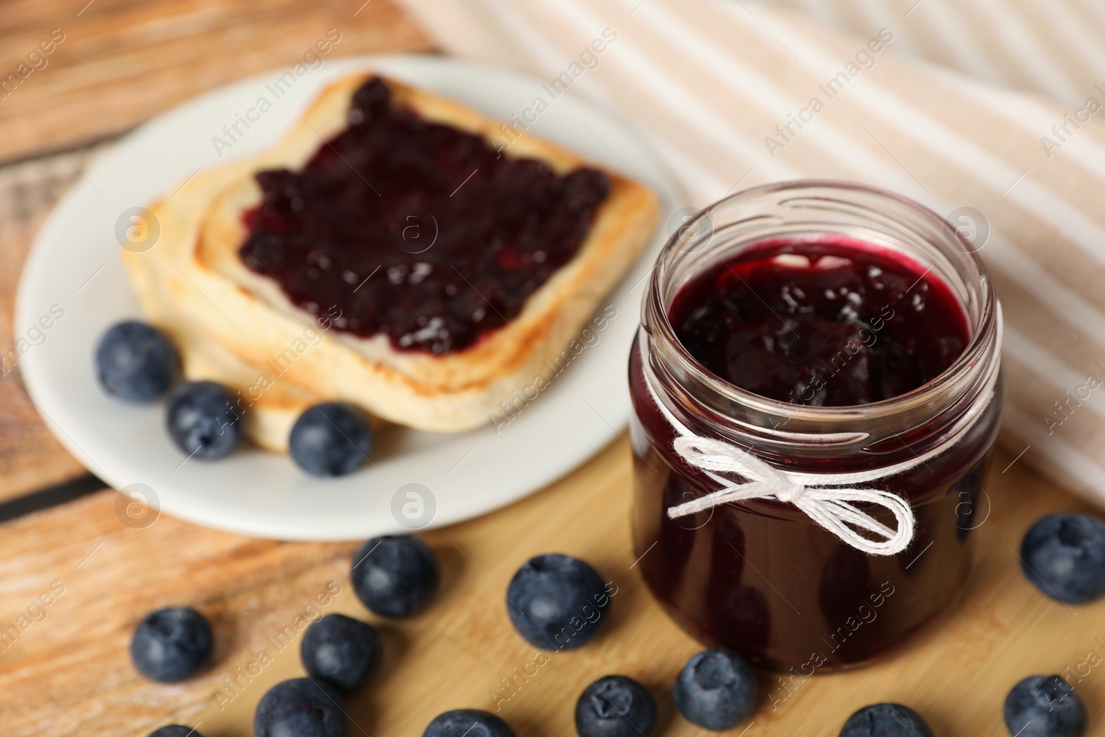 Photo of Jar of delicious blueberry jam and fresh berries on wooden table, closeup. Space for text