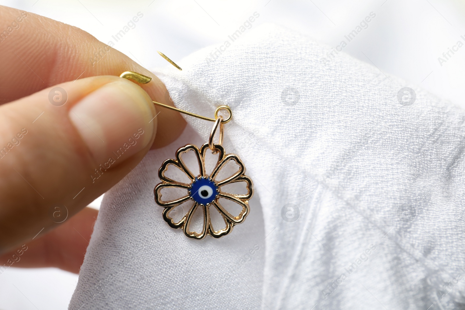 Photo of Woman pinning evil eye amulet on clothing, closeup