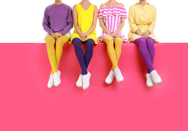 Group of women wearing bright tights and stylish shoes sitting on color background, closeup