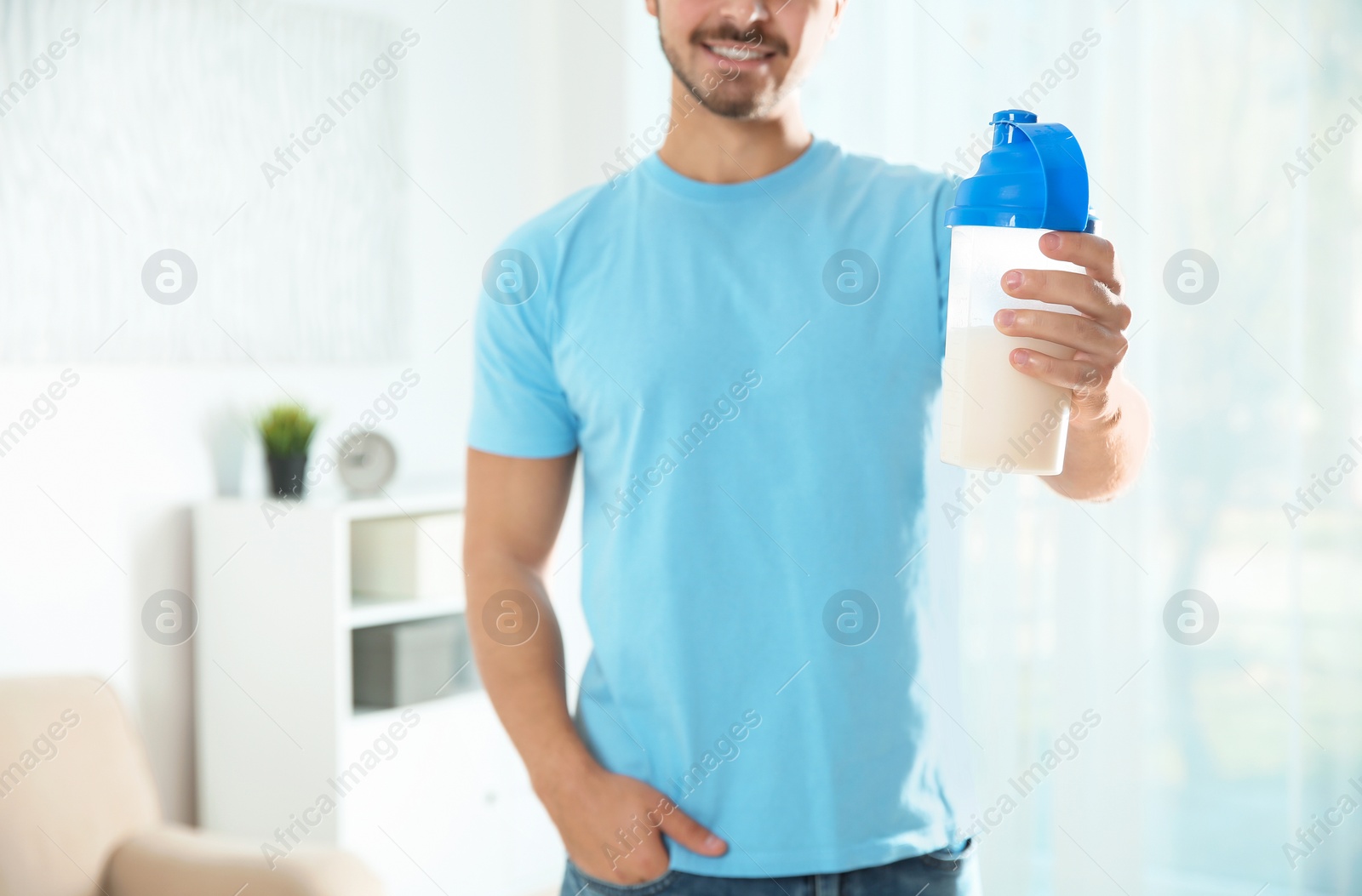 Photo of Young man with bottle of protein shake at home, closeup