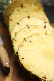 Photo of Tasty cut pineapple and knife on wooden board, closeup