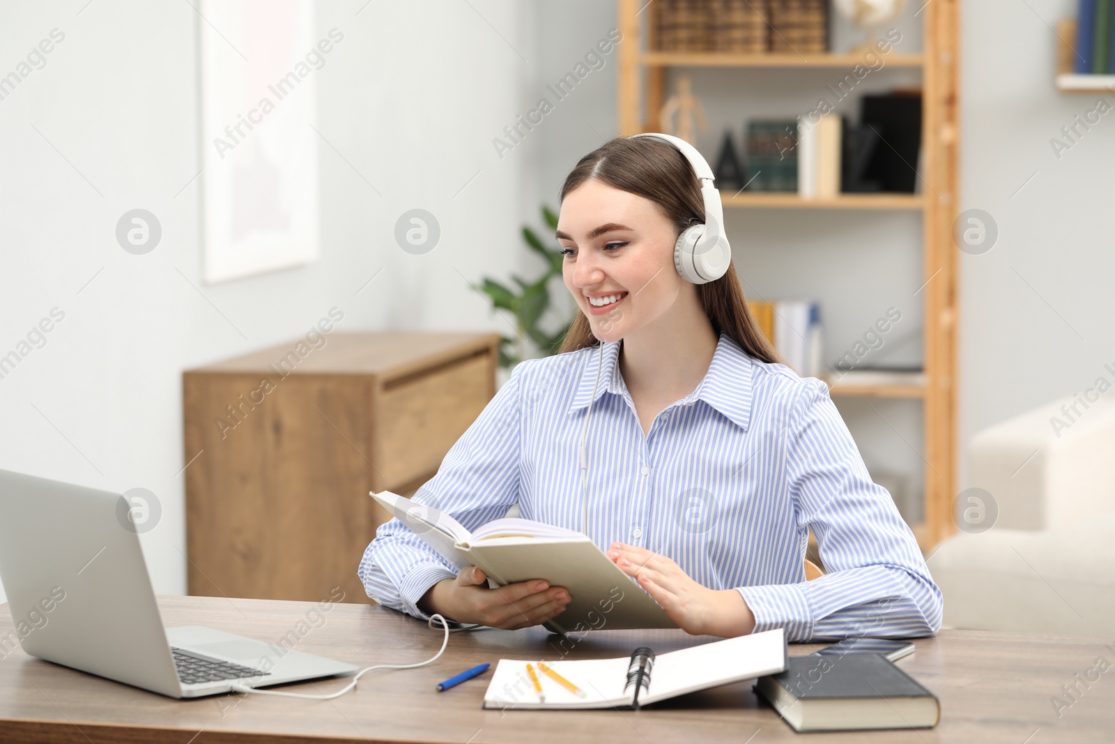 Photo of E-learning. Young woman with book during online lesson at table indoors