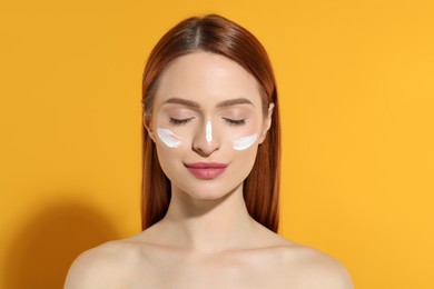 Photo of Beautiful young woman with sun protection cream on her face against orange background