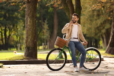 Young man with bicycle drinking coffee in park, space for text