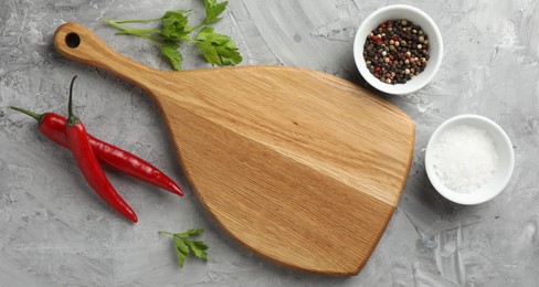 Photo of Cutting board, salt, spices, chili peppers and parsley on grey textured table, flat lay. Space for text