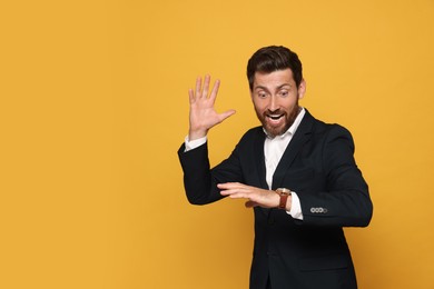 Photo of Emotional man checking time on orange background, space for text. Being late concept