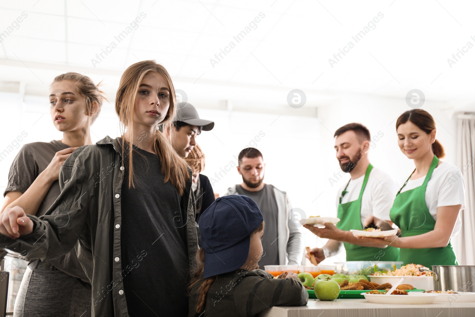 Photo of Teenage girl with other poor people receiving food from volunteers indoors