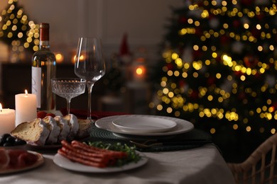 Photo of Christmas table setting with burning candles, appetizers and dishware indoors