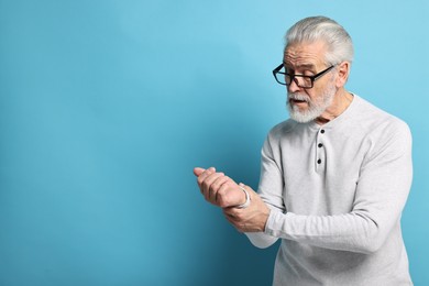 Arthritis symptoms. Man suffering from pain in wrist on light blue background, space for text