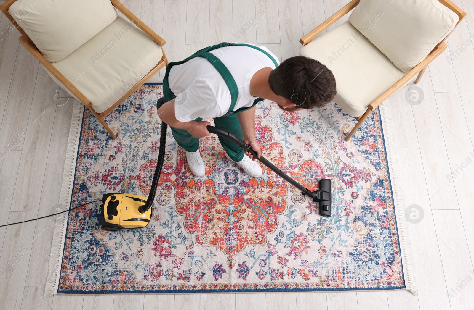 Photo of Dry cleaner's employee hoovering carpet with vacuum cleaner indoors, above view