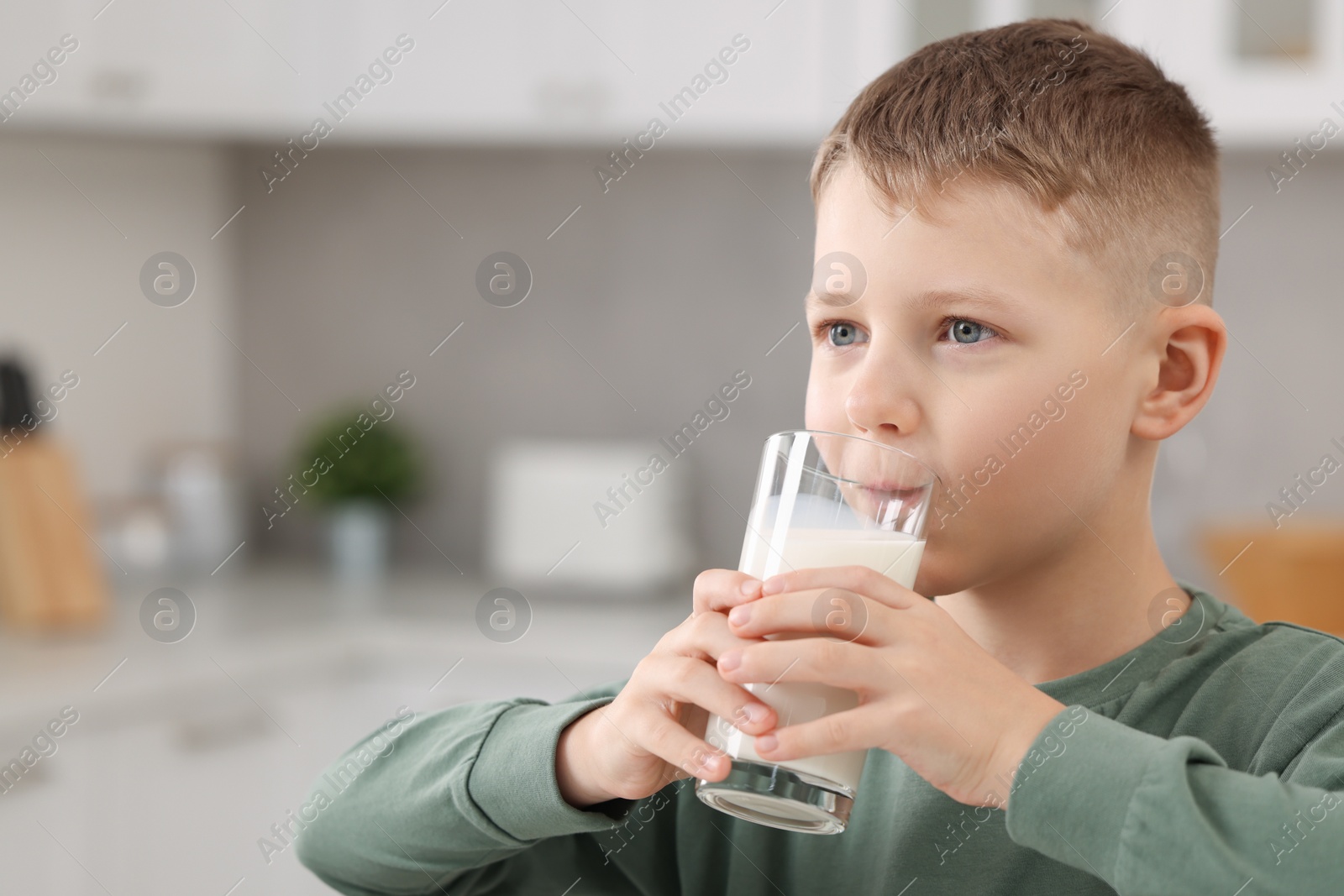 Photo of Cute boy drinking fresh milk from glass indoors, space for text