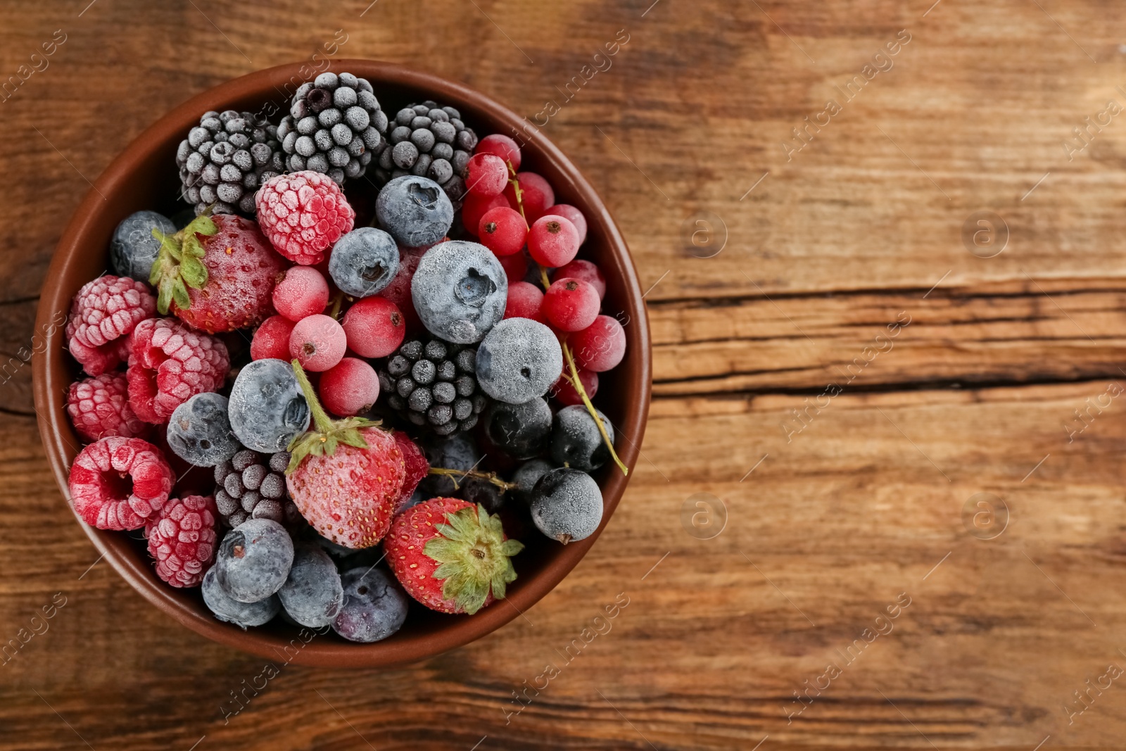 Photo of Mix of different frozen berries in bowl on wooden table, top view. Space for text