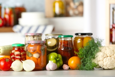 Photo of Fresh vegetables and jars of pickled products on wooden table