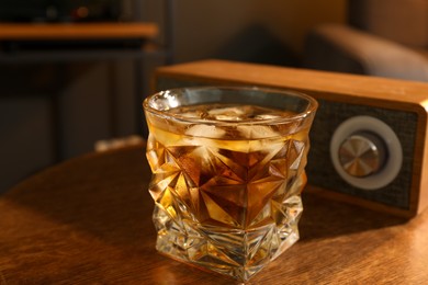 Photo of Glass of whiskey and portable speaker on wooden table in room, closeup. Relax at home