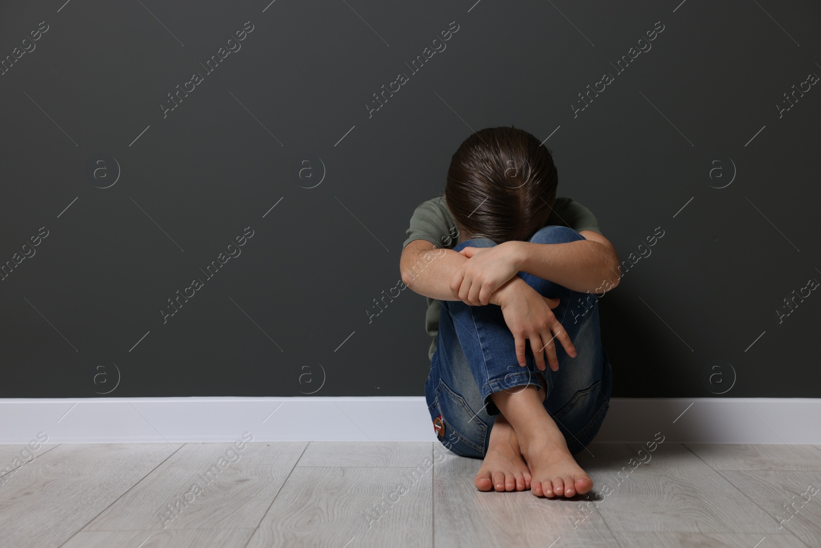 Photo of Child abuse. Upset girl sitting on floor near grey wall, space for text