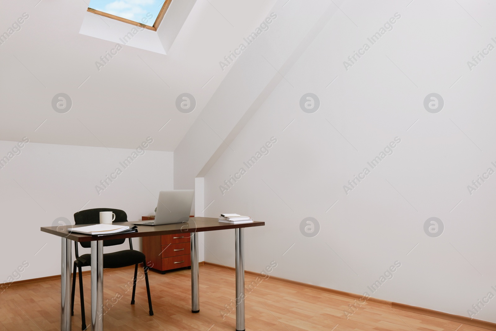 Photo of Stylish workplace with laptop and documents in attic room. Interior design