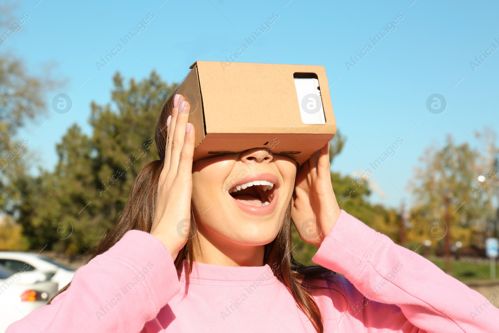 Photo of Young woman using cardboard virtual reality headset outdoors