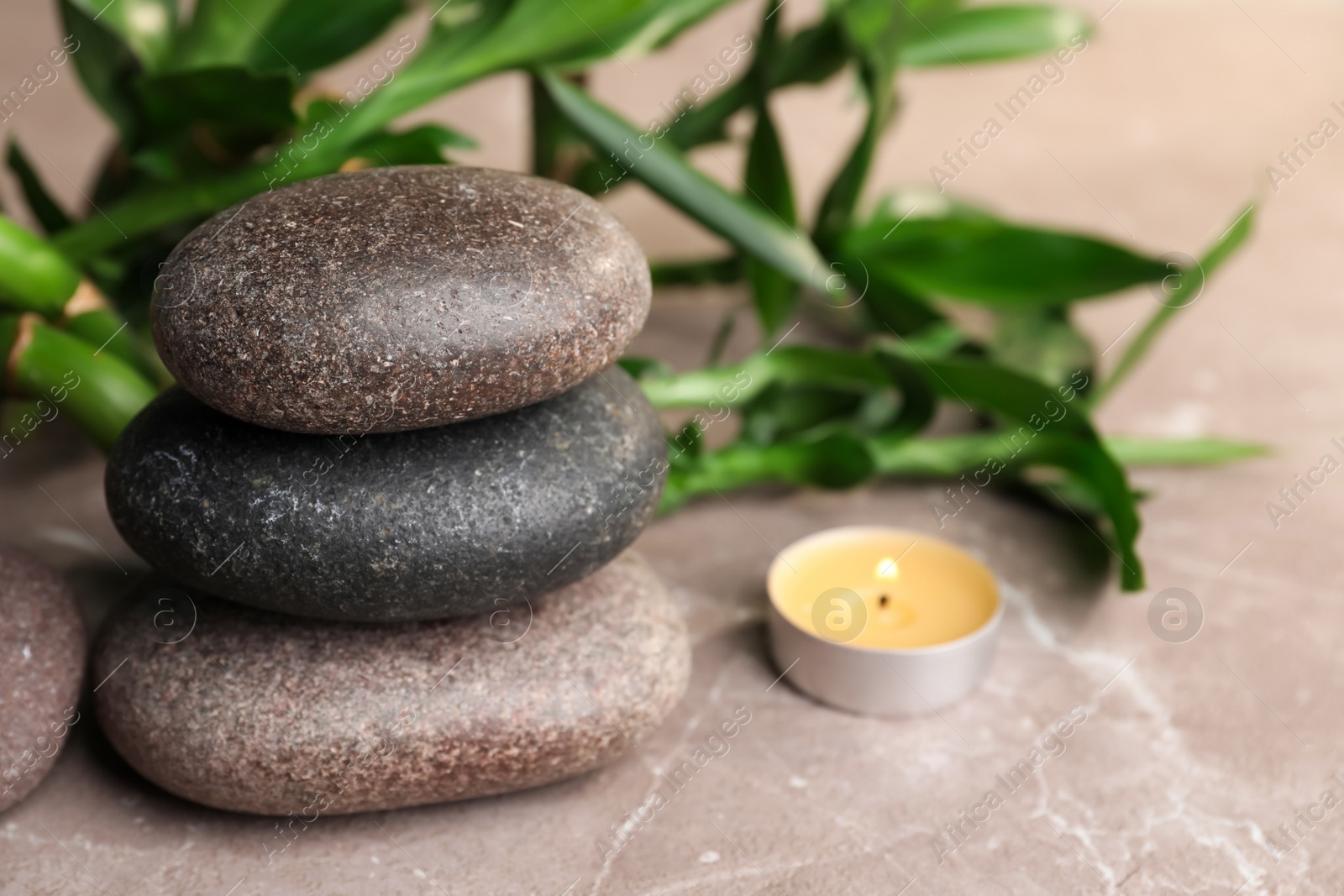 Photo of Stacked spa stones, bamboo and candle on light grey table, closeup