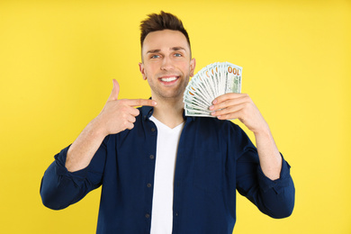 Photo of Happy man with cash money on yellow background