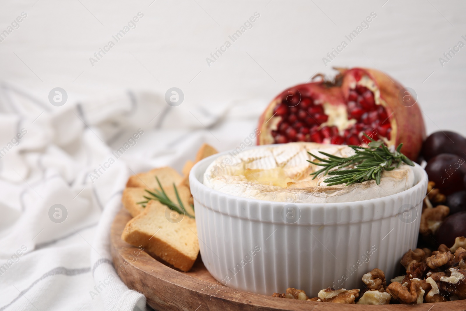Photo of Board with tasty baked camembert, croutons, walnuts and pomegranate on table, closeup. Space for text