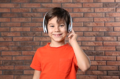 Cute little boy listening to music with headphones against brick wall