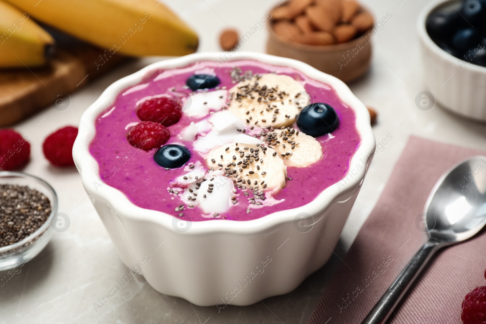 Photo of Delicious acai smoothie with fruits and coconut chips in dessert bowl served on grey table, closeup