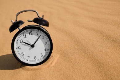 Photo of Black alarm clock on sand in desert. Space for text