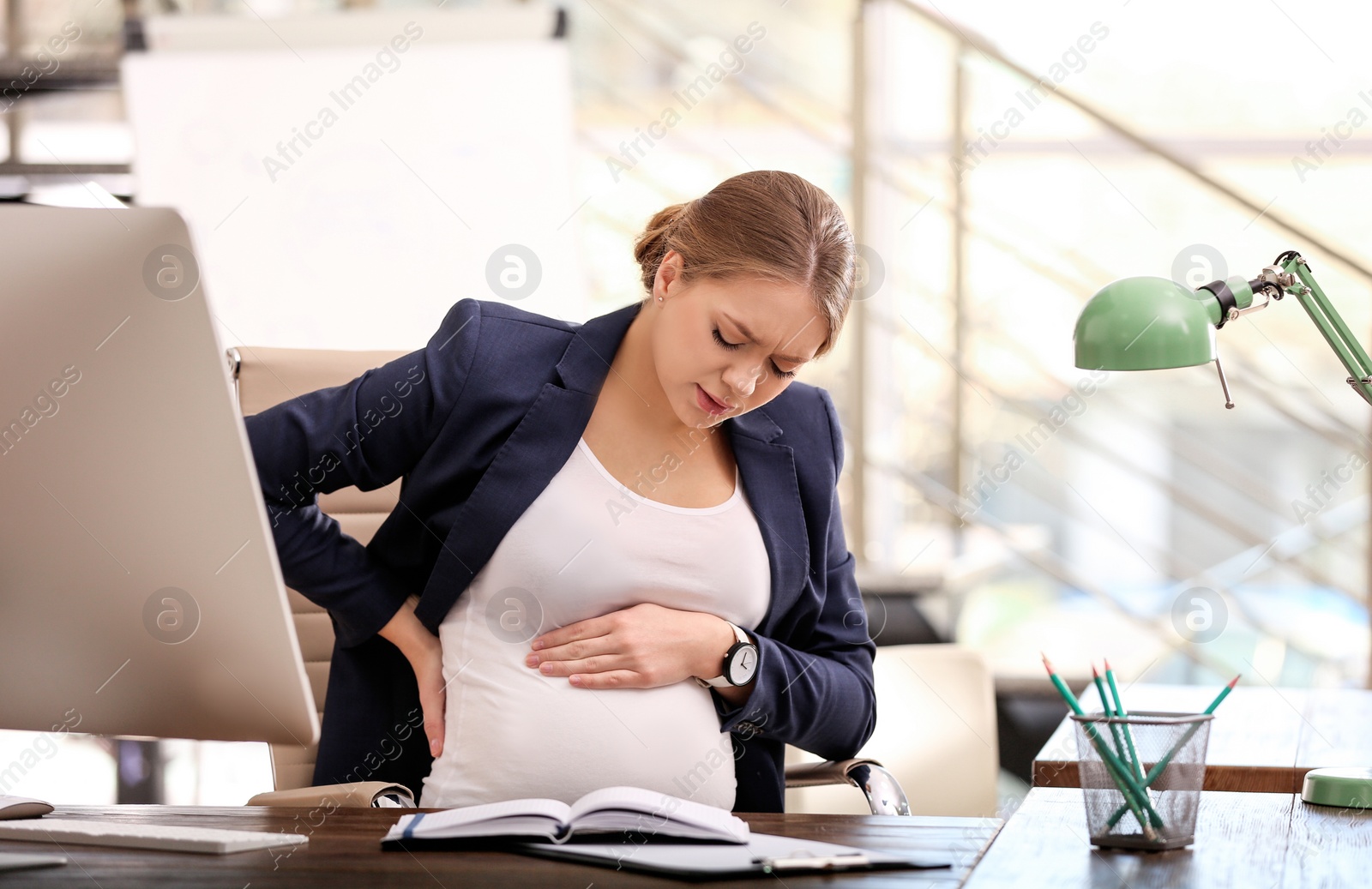 Photo of Young pregnant woman suffering from pain while working in office