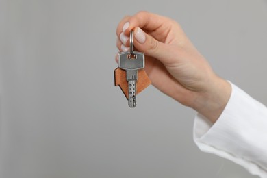 Real estate agent holding key against grey background, closeup