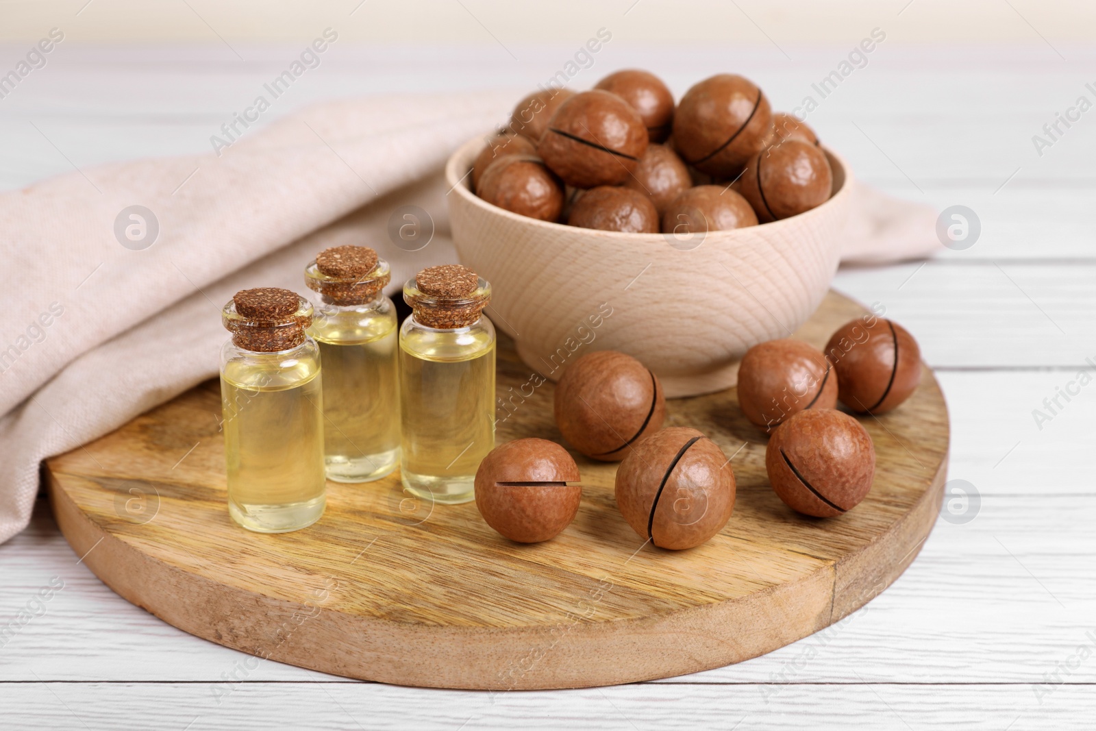 Photo of Delicious organic Macadamia nuts and cosmetic oil on white wooden table