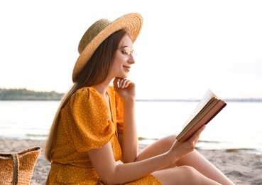 Young woman reading book on sandy beach near sea