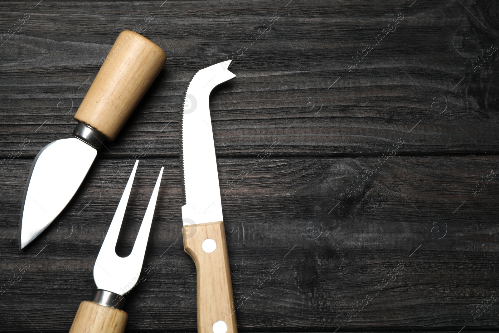 Photo of Cheese knives and fork on black wooden table, flat lay. Space for text