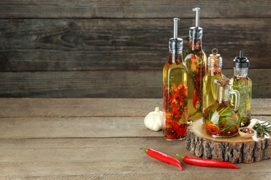 Photo of Cooking oil with different spices and herbs in bottles on wooden table. Space for text