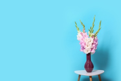 Vase with beautiful gladiolus flowers on wooden table against blue background. Space for text