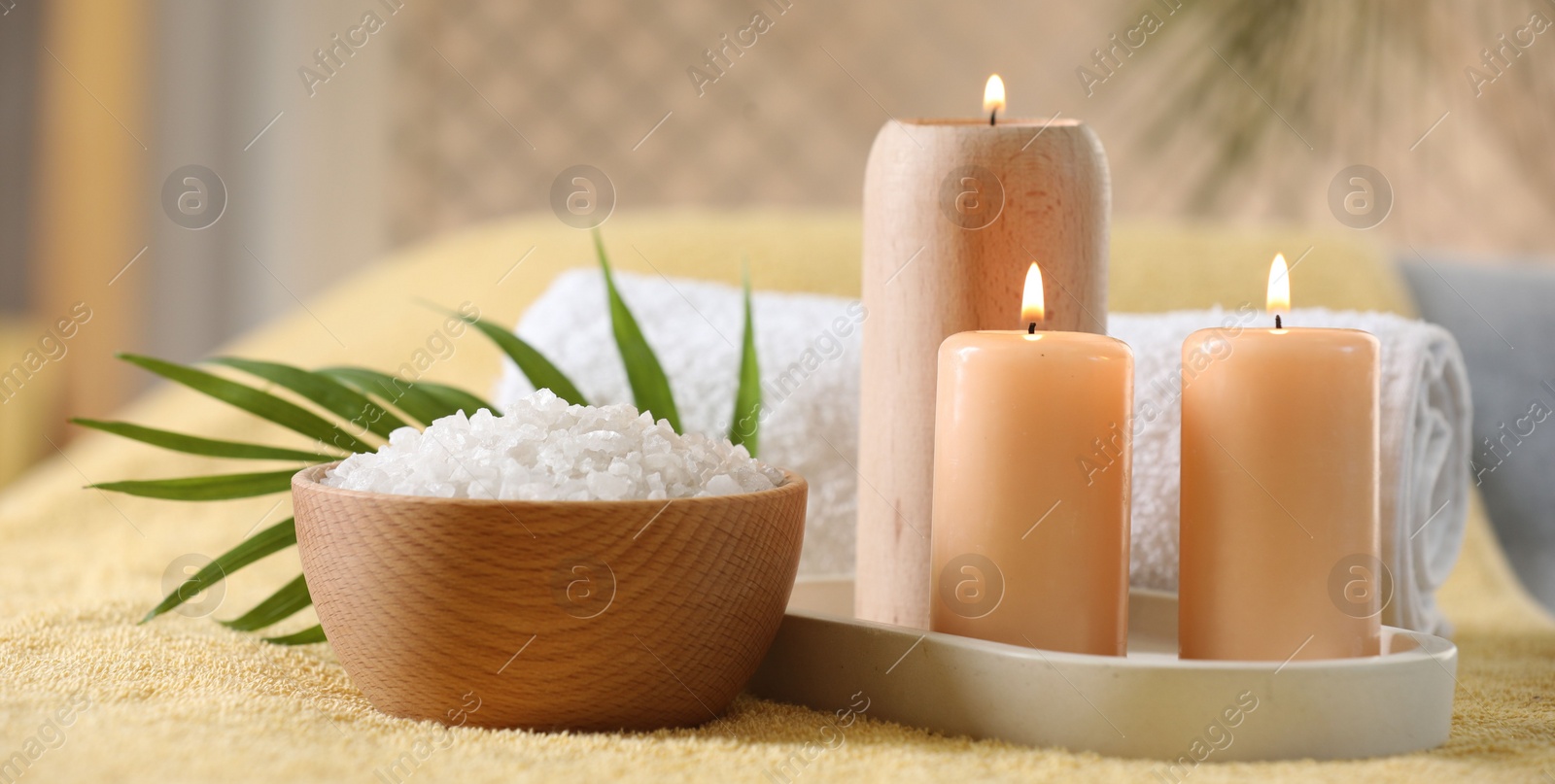 Photo of Spa composition. Burning candles, sea salt and towel on soft yellow surface