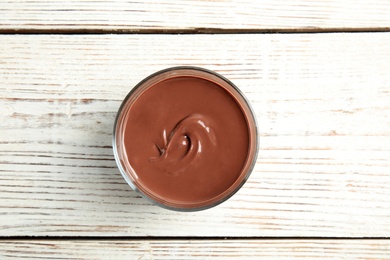 Photo of Glass with tasty chocolate cream on wooden background, top view