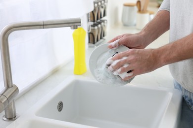 Man washing plate above sink in kitchen, closeup