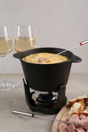 Photo of Fondue pot with tasty melted cheese, forks, wine and different snacks on white table