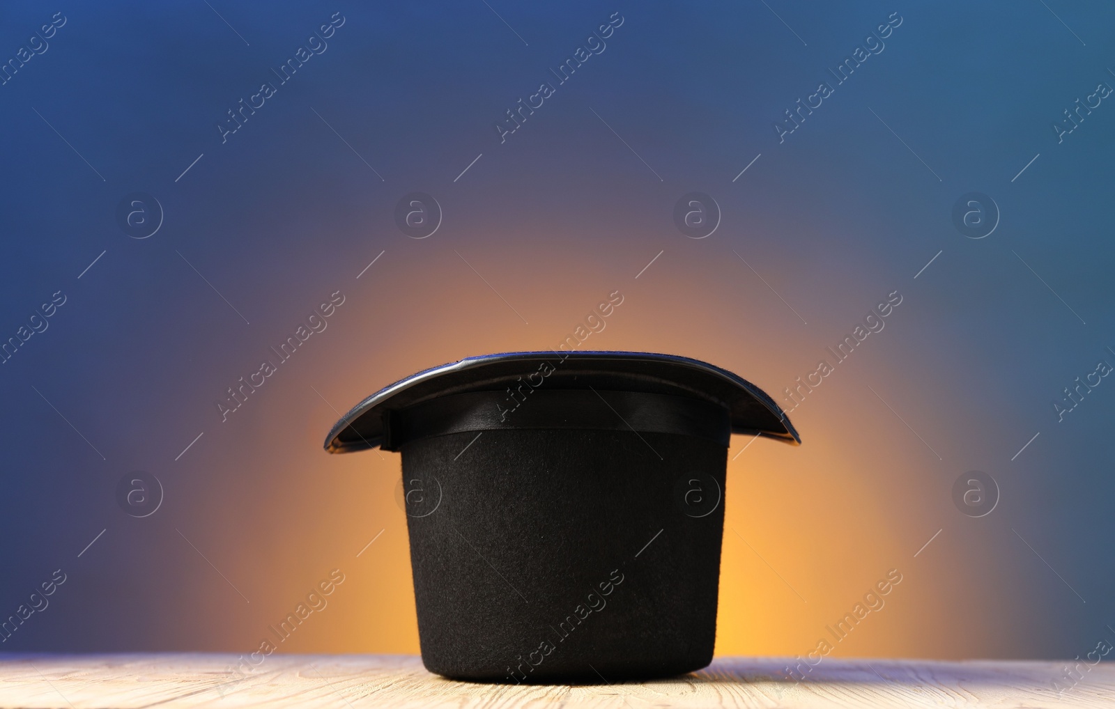 Photo of Magician's hat on wooden table against color background