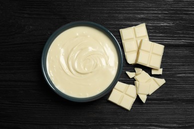 Photo of Tasty white chocolate paste in bowl and pieces on black wooden table, top view