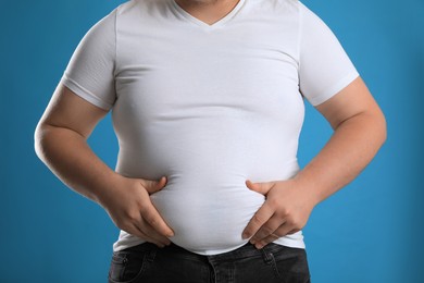 Photo of Overweight man in tight t-shirt on light blue background, closeup