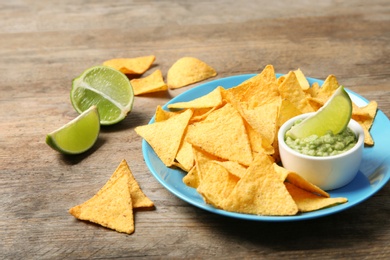 Plate with delicious mexican nachos chips, guacamole sauce and lime on wooden table