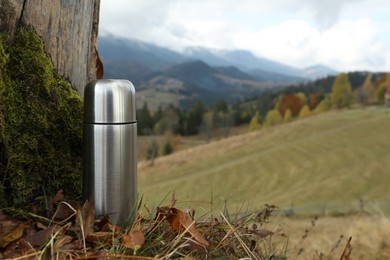 Photo of Silver thermos near tree in mountains, space for text