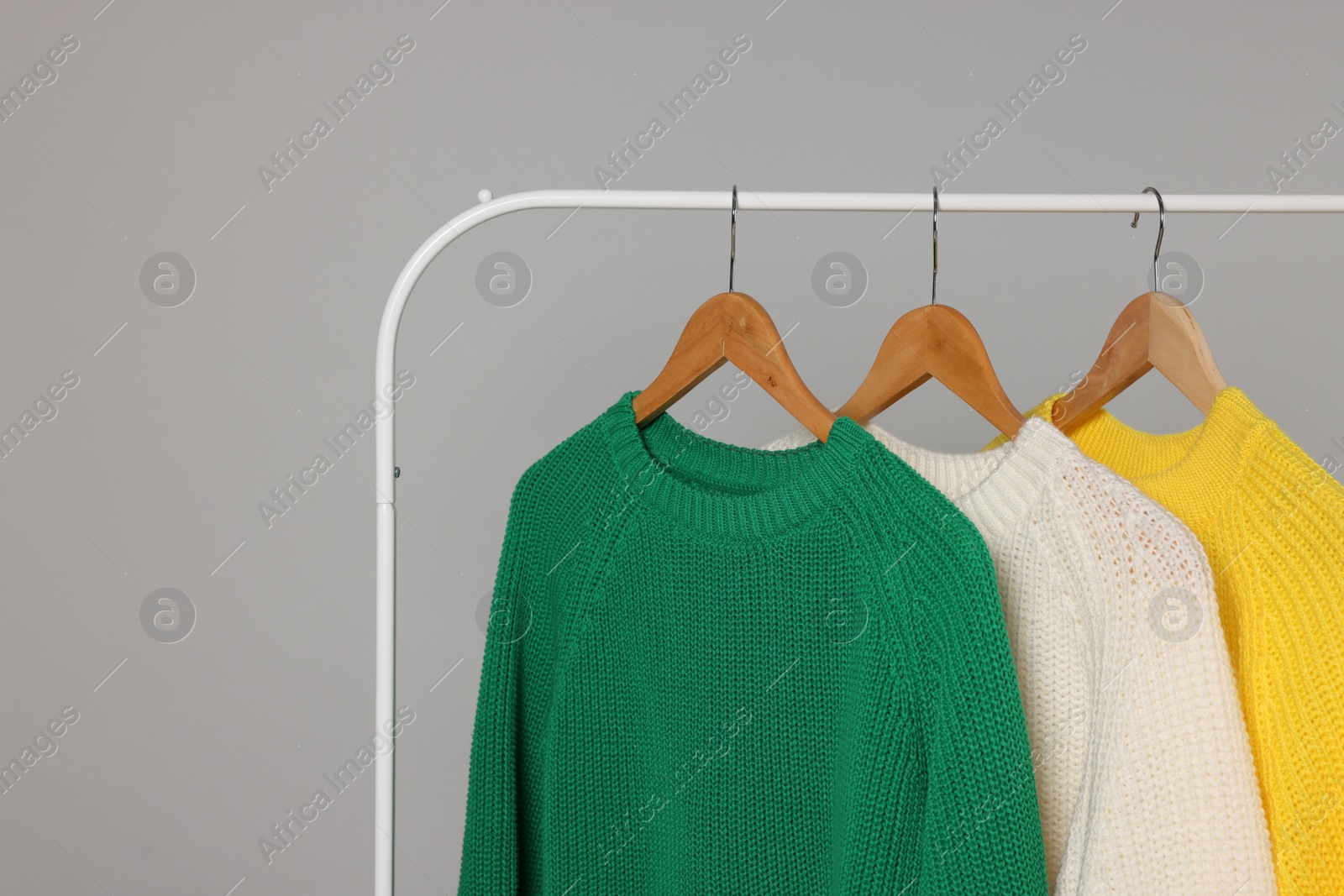 Photo of Rack with different warm sweaters on light grey background, space for text