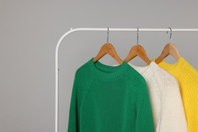 Photo of Rack with different warm sweaters on light grey background, space for text