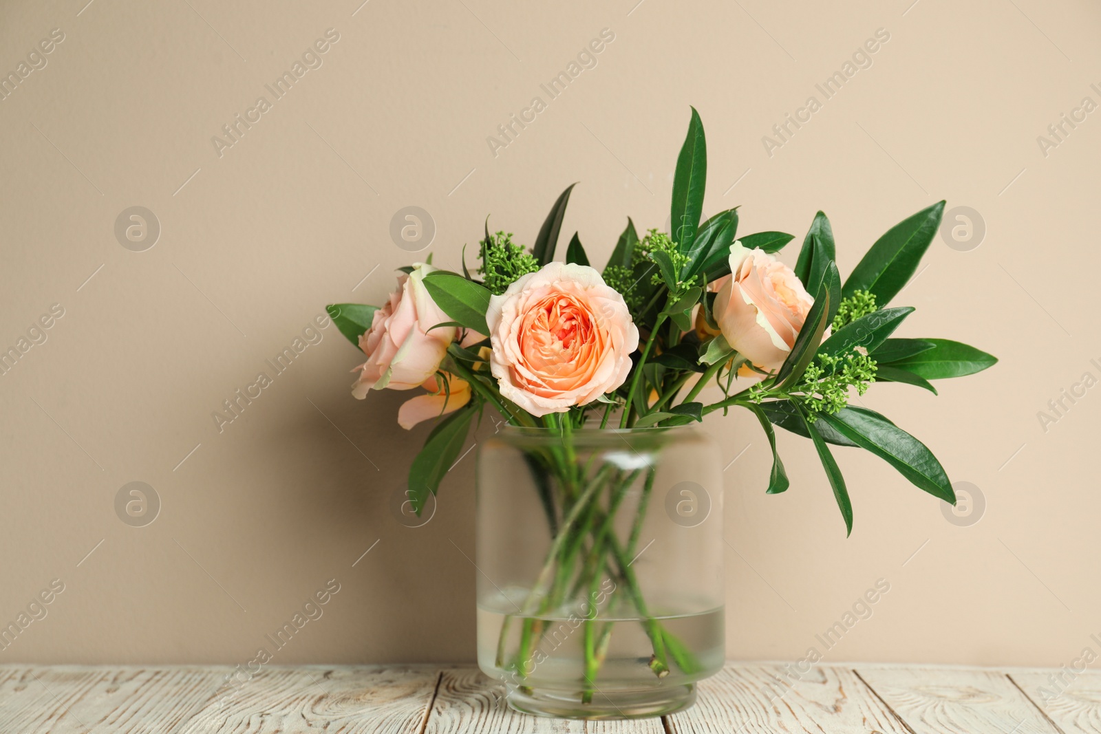 Photo of Bouquet with beautiful flowers in glass vase on light wooden table against beige background