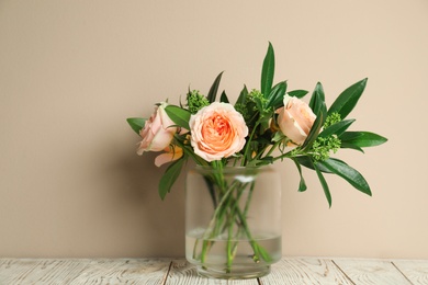 Bouquet with beautiful flowers in glass vase on light wooden table against beige background