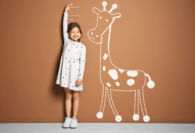 Image of Little girl measuring height and drawing of giraffe near brown wall