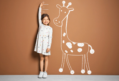 Little girl measuring height and drawing of giraffe near brown wall